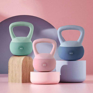 Colorful fitness equipment: Assortment of pastel-colored kettlebells of different weights displayed on wood and concrete blocks against a pink background.