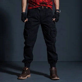 Rugged black cargo pants with multiple pockets, worn by a person in a red patterned shirt and dark boots, set against a dark background.