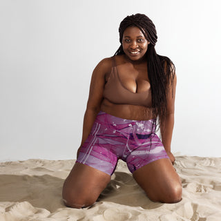 High-waist purple patterned shorts worn by a smiling Black woman with long dreadlocks on a sand-filled background.