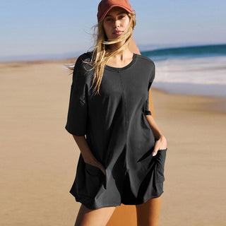 Casual beach outfit with black loose-fitting dress and orange baseball cap on woman standing on sandy shore