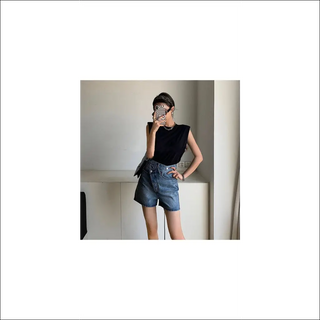 Black sleeveless top, distressed denim shorts, and stylish sunglasses worn by a young female model in a minimalist setting.