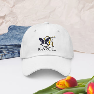 White stylish dad cap with the K-AROLE logo embroidered on the front, placed in a fashionable setting with denim and tulips.