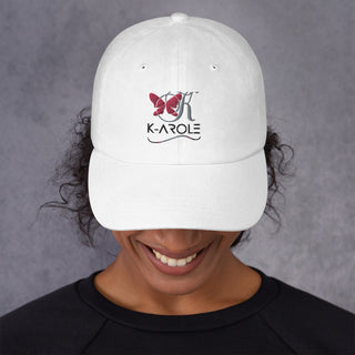 White K-AROLE branded dad hat with a red butterfly logo, worn by a smiling woman with curly dark hair against a gray background.