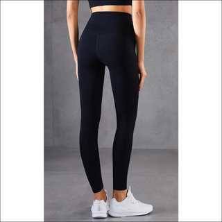 Sleek high-waisted black activewear leggings showcased on a female model in a fitness studio setting. The slim-fitting, stretchy pants feature a stylish silhouette and are designed for versatile athletic or casual wear.