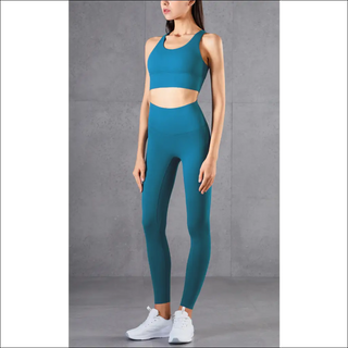 Sleek, teal blue athletic crop top and leggings set showcasing modern, stretchy fitness attire on a slim, active woman against a plain grey background.