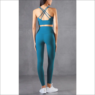 Turquoise sports bra and leggings with crisscross back straps, worn by a woman against a gray background