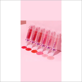 Assortment of vibrant, glossy lip colors in tubes on a pastel pink background