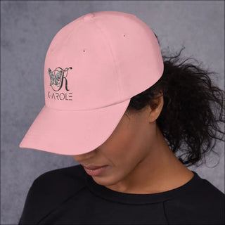 Pink fashion cap with K-AROLE logo and butterfly graphic, worn by a person with curly dark hair against a gray background