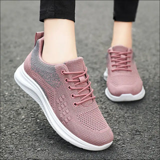 Light and breathable pink knit sneakers with lace-up design, worn by a person with black pants, providing a stylish and comfortable footwear option.