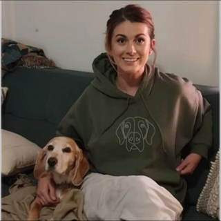 Smiling woman wearing cozy green hoodie, sitting with adorable dog on couch