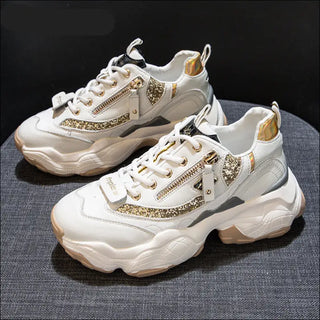 Stylish women's sneakers with golden accents. The chunky, white sneakers feature lace-up closures, side zippers, and metallic gold details that add a touch of glamour. The textured, platform soles provide a trendy, elevated look.